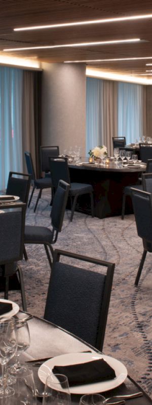 The image shows an elegantly set-up banquet hall with round tables, black chairs, and white floral centerpieces, ready for an event or gathering.