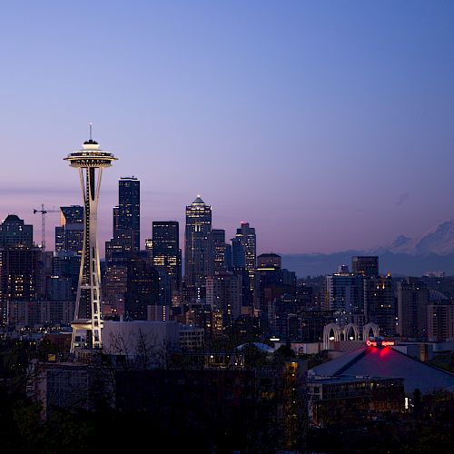 This image shows the Seattle skyline at dusk, with the Space Needle prominent in the foreground and Mount Rainier visible in the background.
